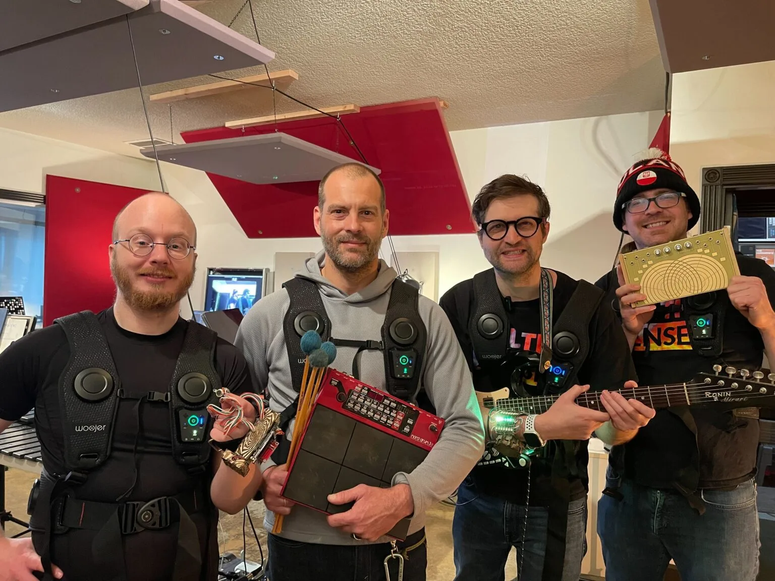 Four people wearing haptic vests and lit wearable bracers at a Haptic Zoo demo, one holding a brass circuit board